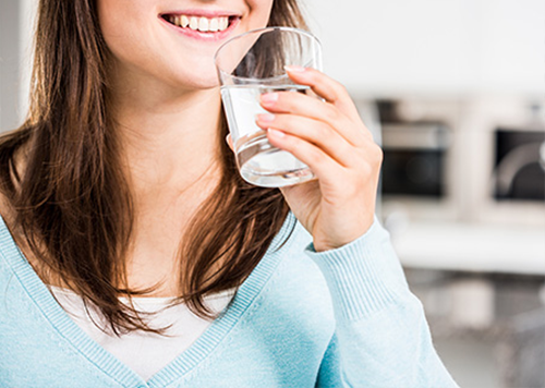 Junge Frau trinkt ein Glas Wasser gegen Husten.